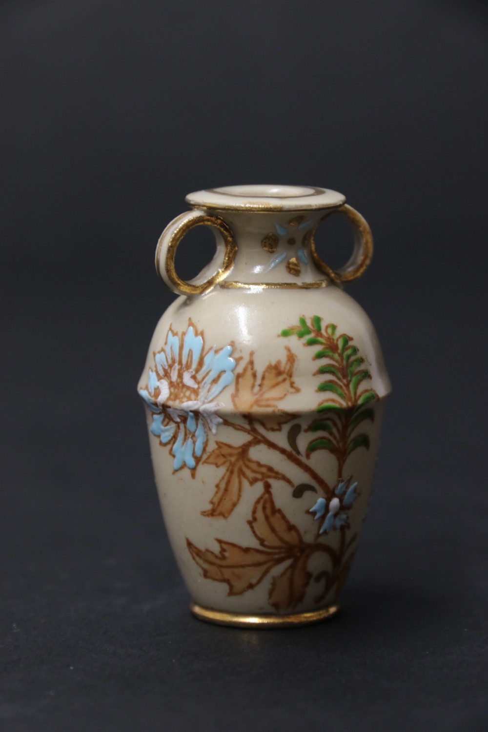 A set of three antique miniature cream ceramic vases featuring hand-painted floral motifs in blue, green, and brown with gilded highlights. View XVII