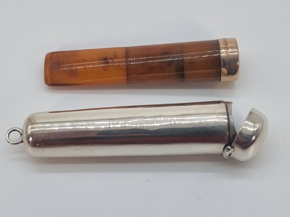 An Edwardian amber cheroot holder with a gold rim positioned next to its hallmarked sterling silver protective case.