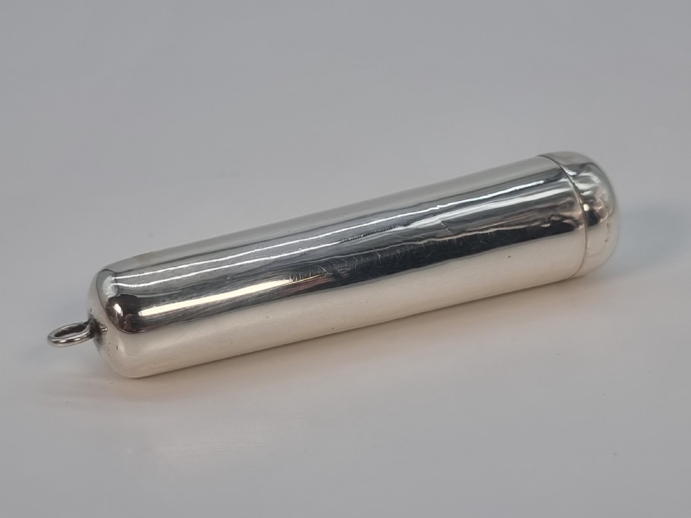 An Edwardian amber cheroot holder with a gold rim positioned next to its hallmarked sterling silver protective case. View III