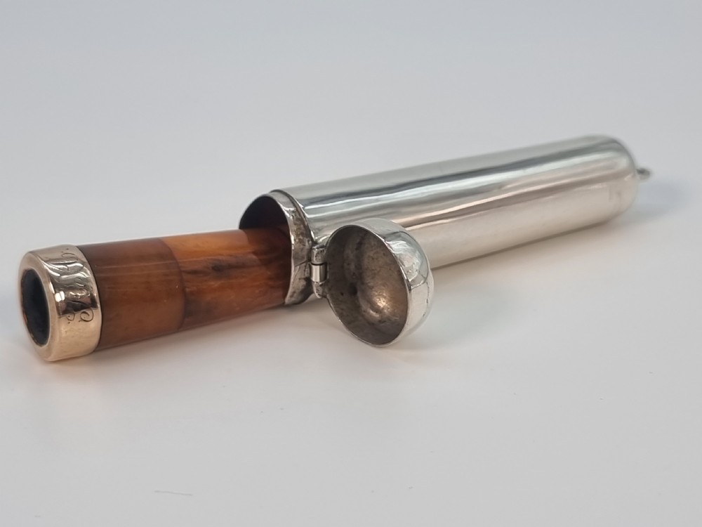 An Edwardian amber cheroot holder with a gold rim positioned next to its hallmarked sterling silver protective case. View VI