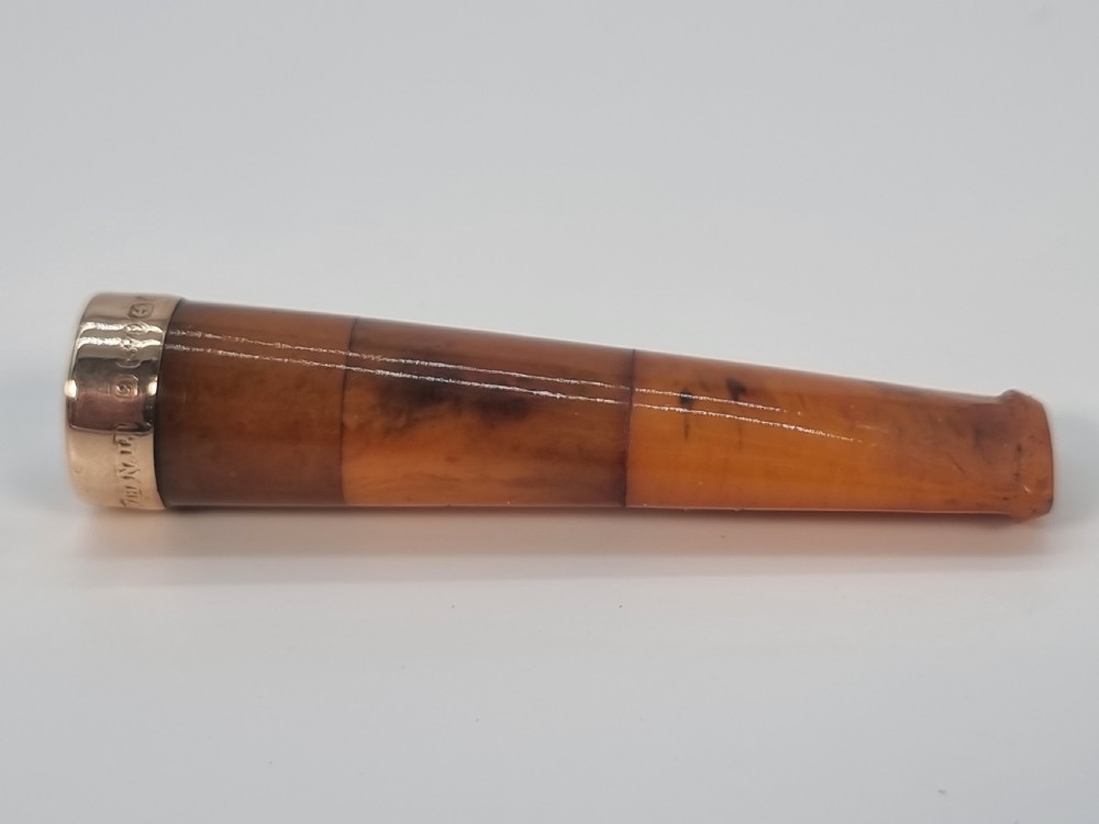 An Edwardian amber cheroot holder with a gold rim positioned next to its hallmarked sterling silver protective case. View VIII