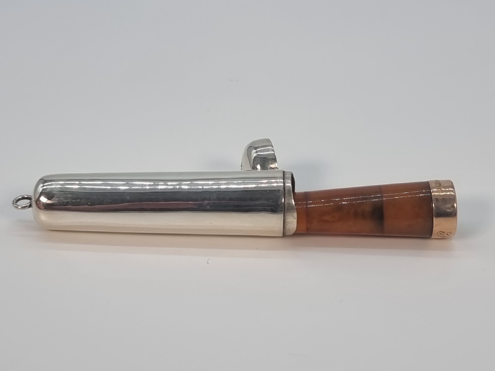 An Edwardian amber cheroot holder with a gold rim positioned next to its hallmarked sterling silver protective case. View X
