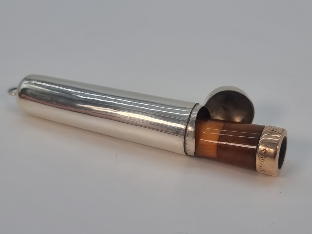 An Edwardian amber cheroot holder with a gold rim positioned next to its hallmarked sterling silver protective case. View XII