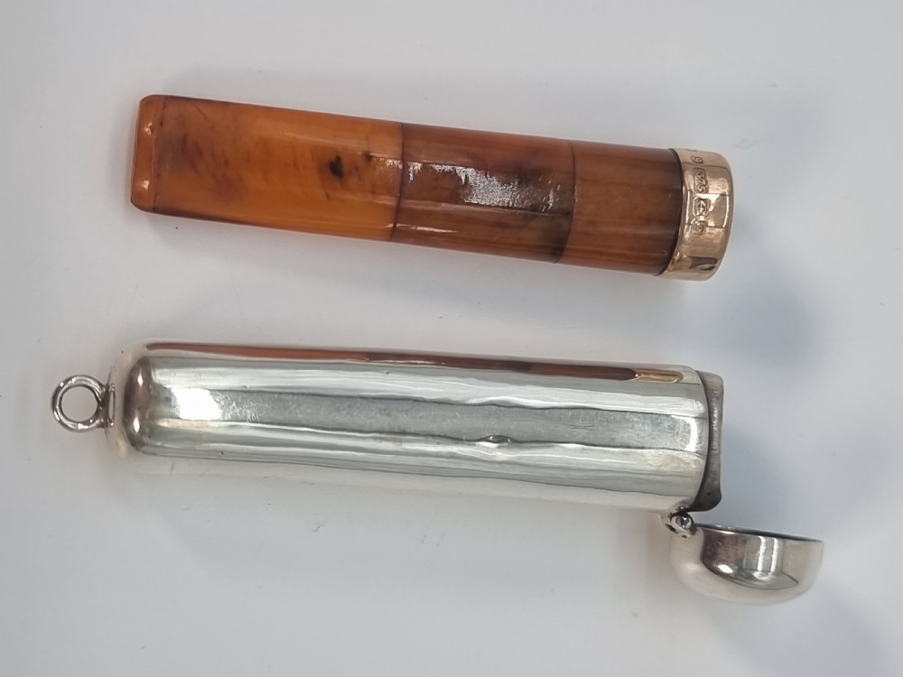 An Edwardian amber cheroot holder with a gold rim positioned next to its hallmarked sterling silver protective case. View XVIII