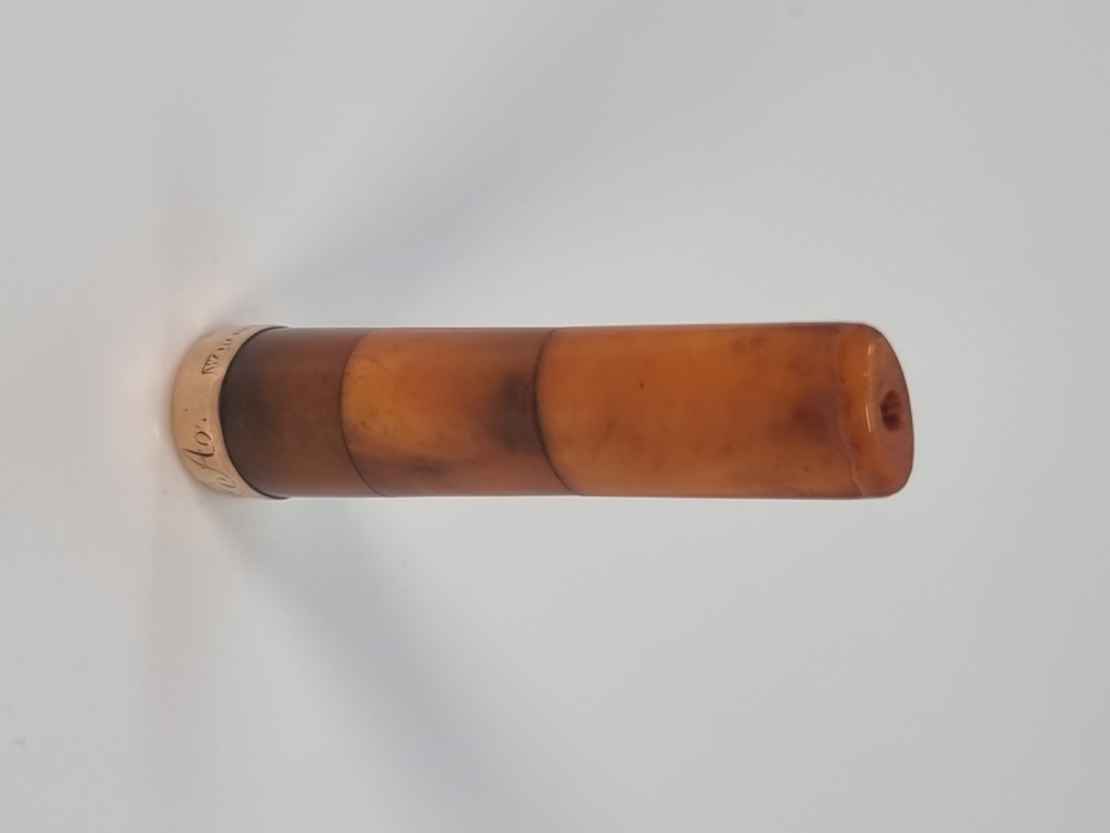 An Edwardian amber cheroot holder with a gold rim positioned next to its hallmarked sterling silver protective case. View XXIII