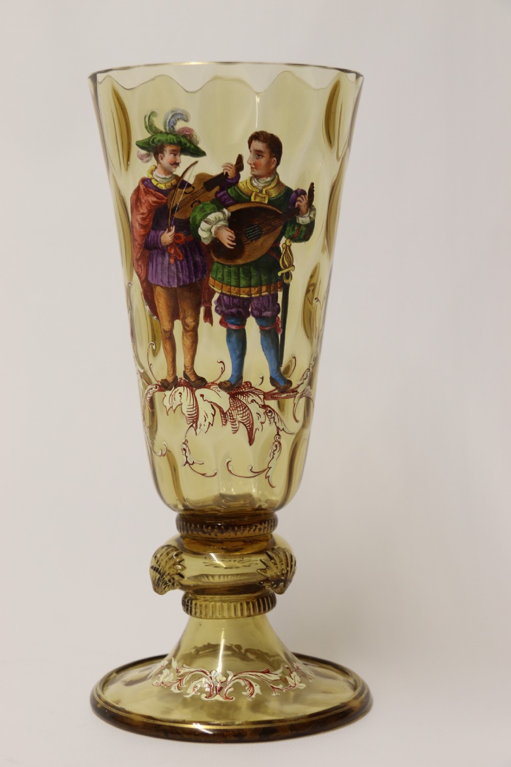 A pair of tall amber glass goblets featuring hand-painted enamelled figures of Renaissance musicians with scalloped rims and decorative knopped stems. View III