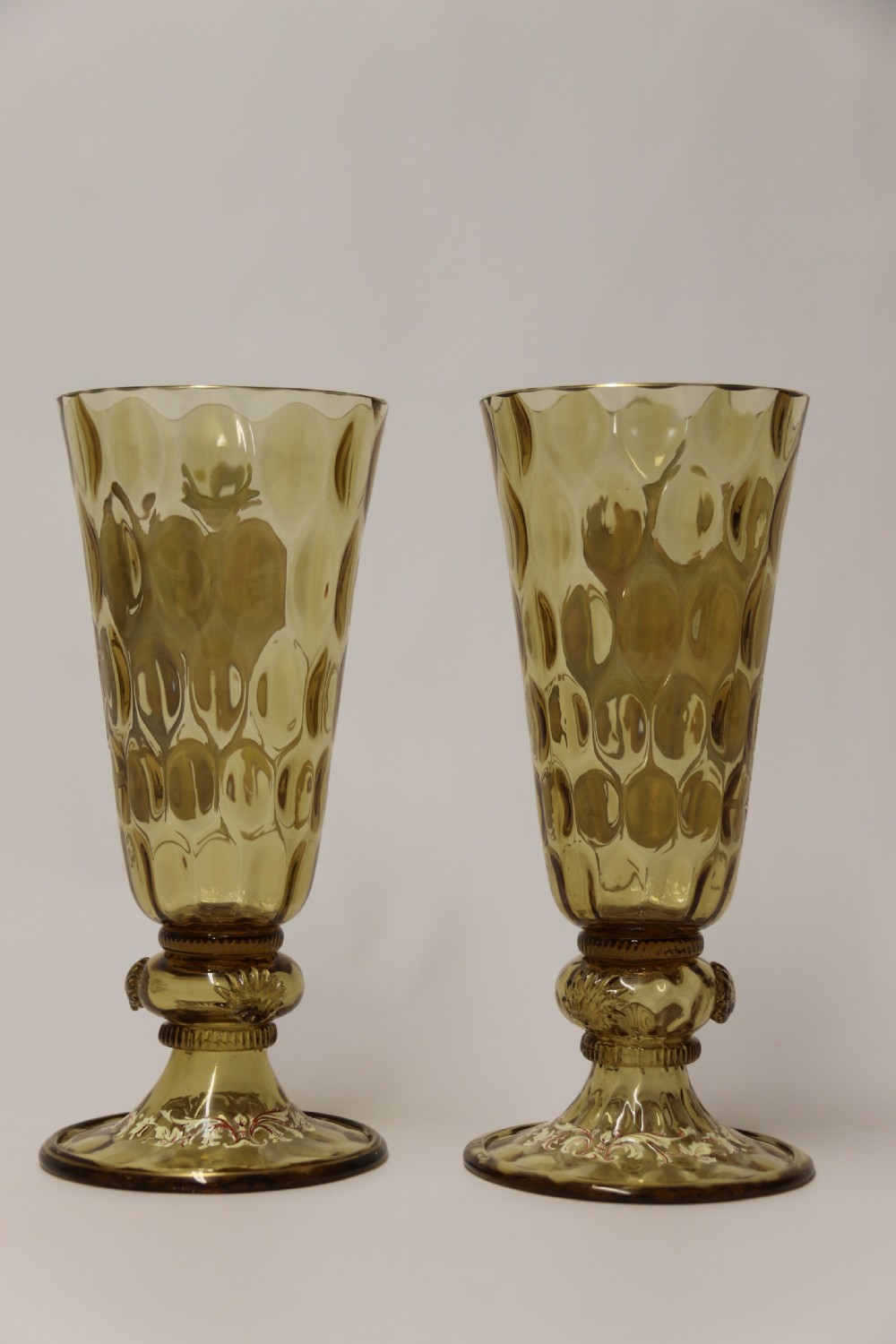 A pair of tall amber glass goblets featuring hand-painted enamelled figures of Renaissance musicians with scalloped rims and decorative knopped stems. View XII