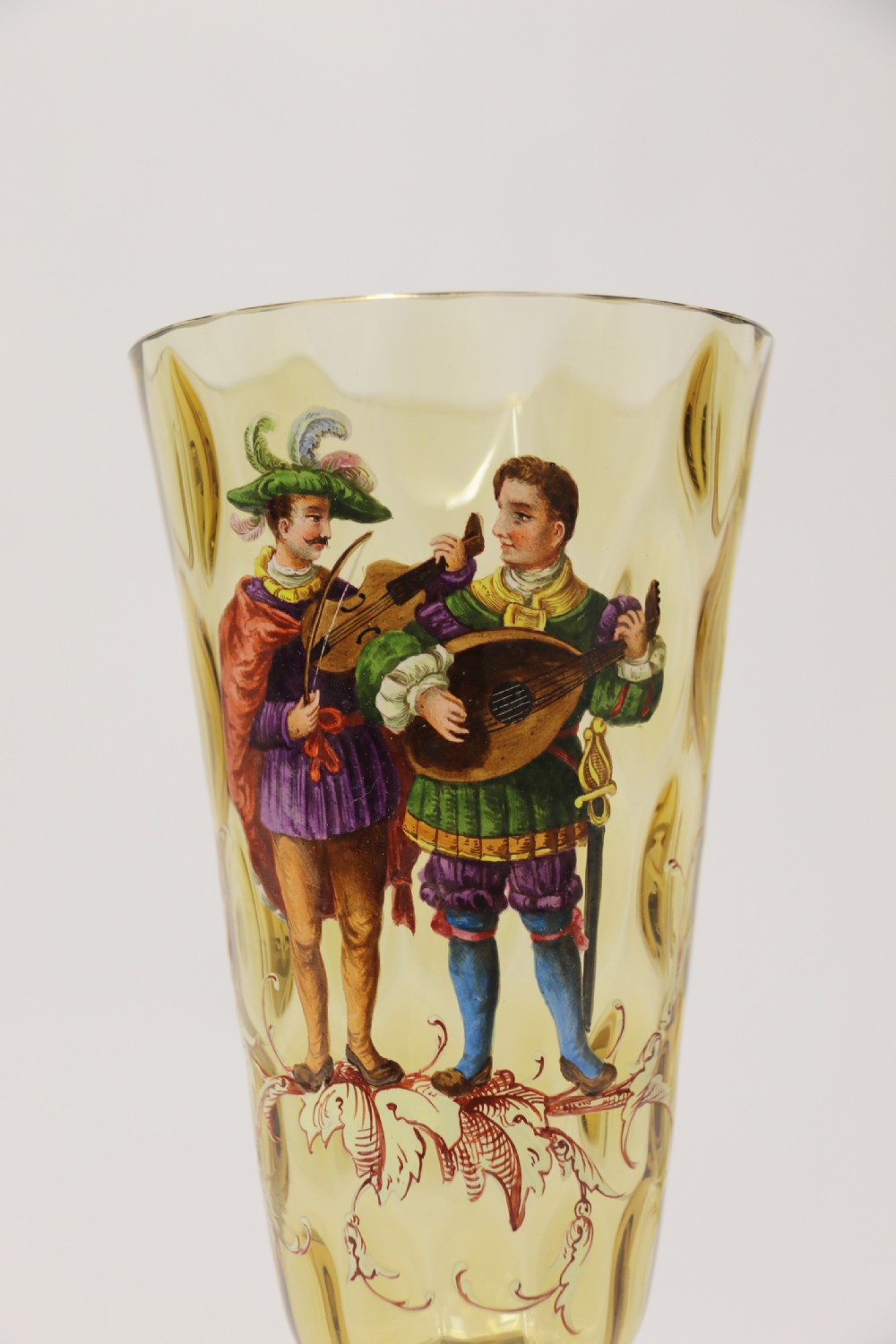 A pair of tall amber glass goblets featuring hand-painted enamelled figures of Renaissance musicians with scalloped rims and decorative knopped stems. View XIII