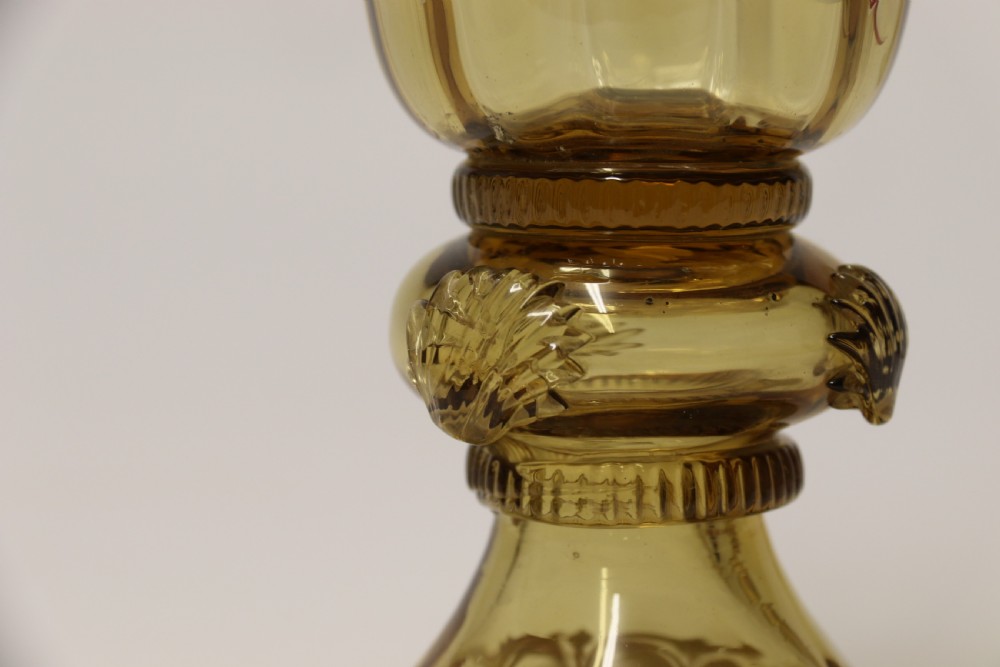 A pair of tall amber glass goblets featuring hand-painted enamelled figures of Renaissance musicians with scalloped rims and decorative knopped stems. View XV
