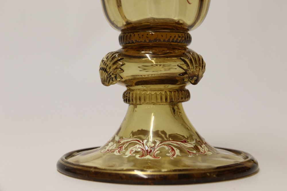 A pair of tall amber glass goblets featuring hand-painted enamelled figures of Renaissance musicians with scalloped rims and decorative knopped stems. View XVI