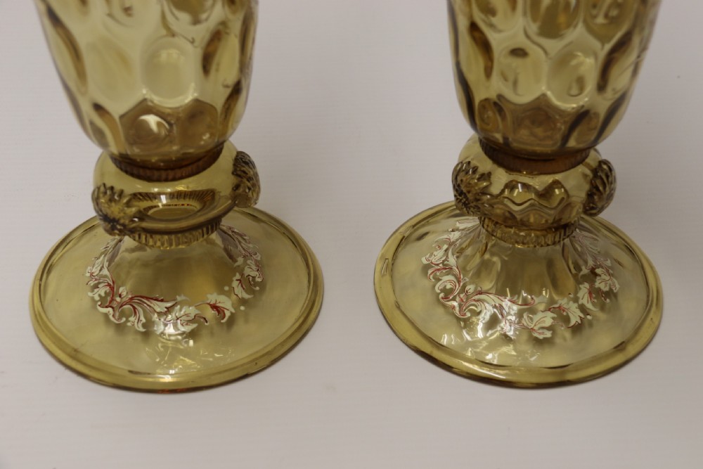A pair of tall amber glass goblets featuring hand-painted enamelled figures of Renaissance musicians with scalloped rims and decorative knopped stems. View XXI