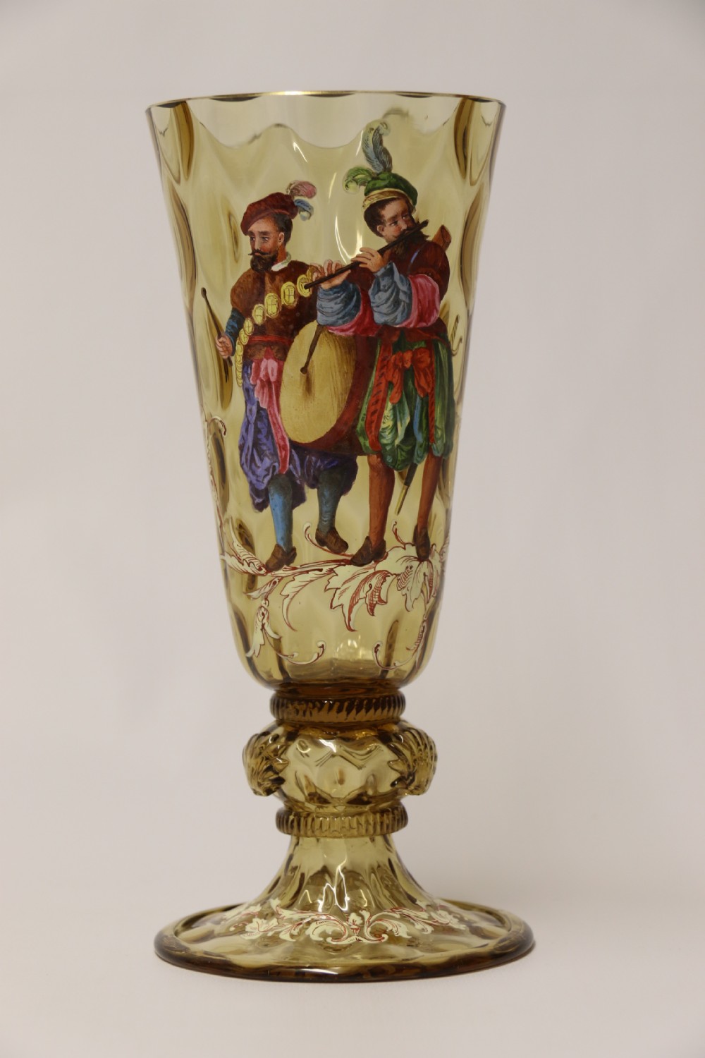 A pair of tall amber glass goblets featuring hand-painted enamelled figures of Renaissance musicians with scalloped rims and decorative knopped stems. View XXIII