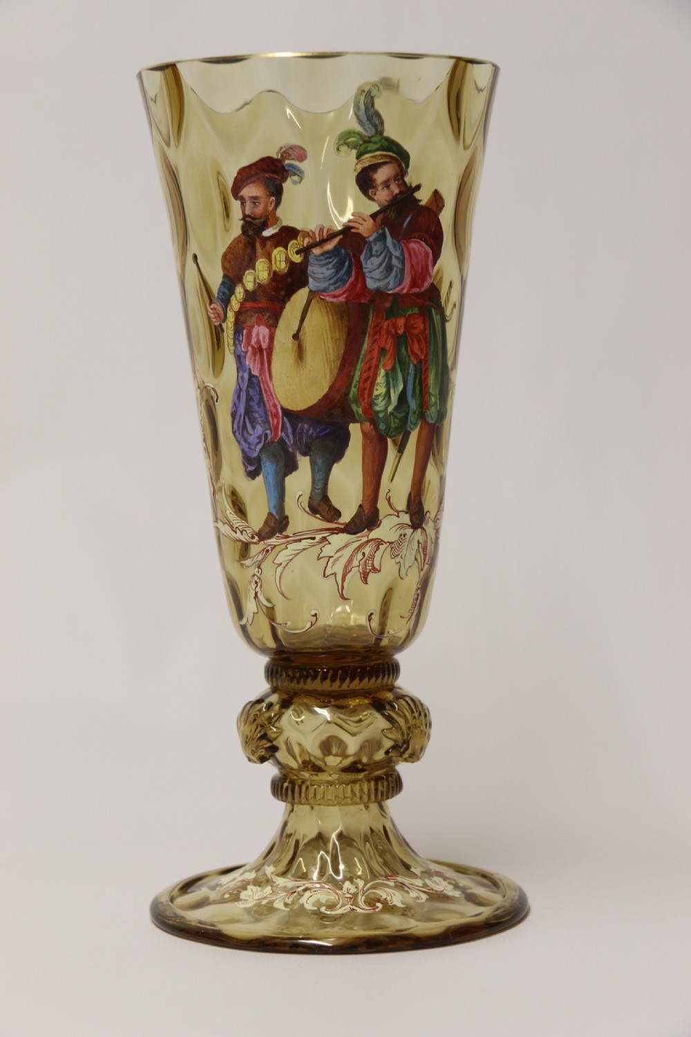 A pair of tall amber glass goblets featuring hand-painted enamelled figures of Renaissance musicians with scalloped rims and decorative knopped stems. View XXIV