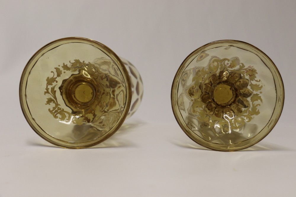 A pair of tall amber glass goblets featuring hand-painted enamelled figures of Renaissance musicians with scalloped rims and decorative knopped stems. View XXX