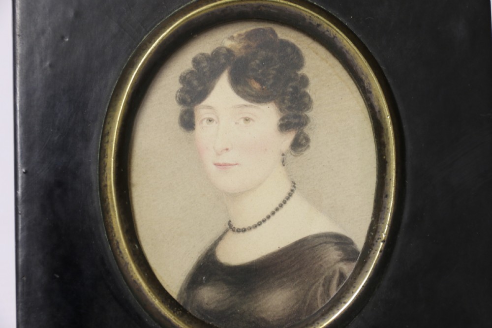 An English Regency period oval watercolour portrait miniature of a lady with dark hair, set in a rectangular black ebonised frame with a brass leaf hanger mount. View III