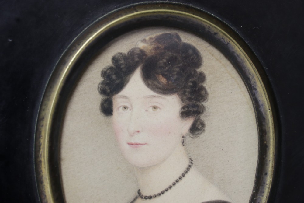An English Regency period oval watercolour portrait miniature of a lady with dark hair, set in a rectangular black ebonised frame with a brass leaf hanger mount. View IV