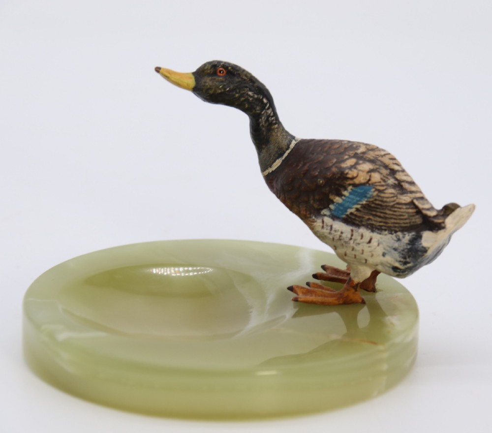 A cold painted bronze study of a mallard duck standing on the rim of a dished, circular green onyx base. View II