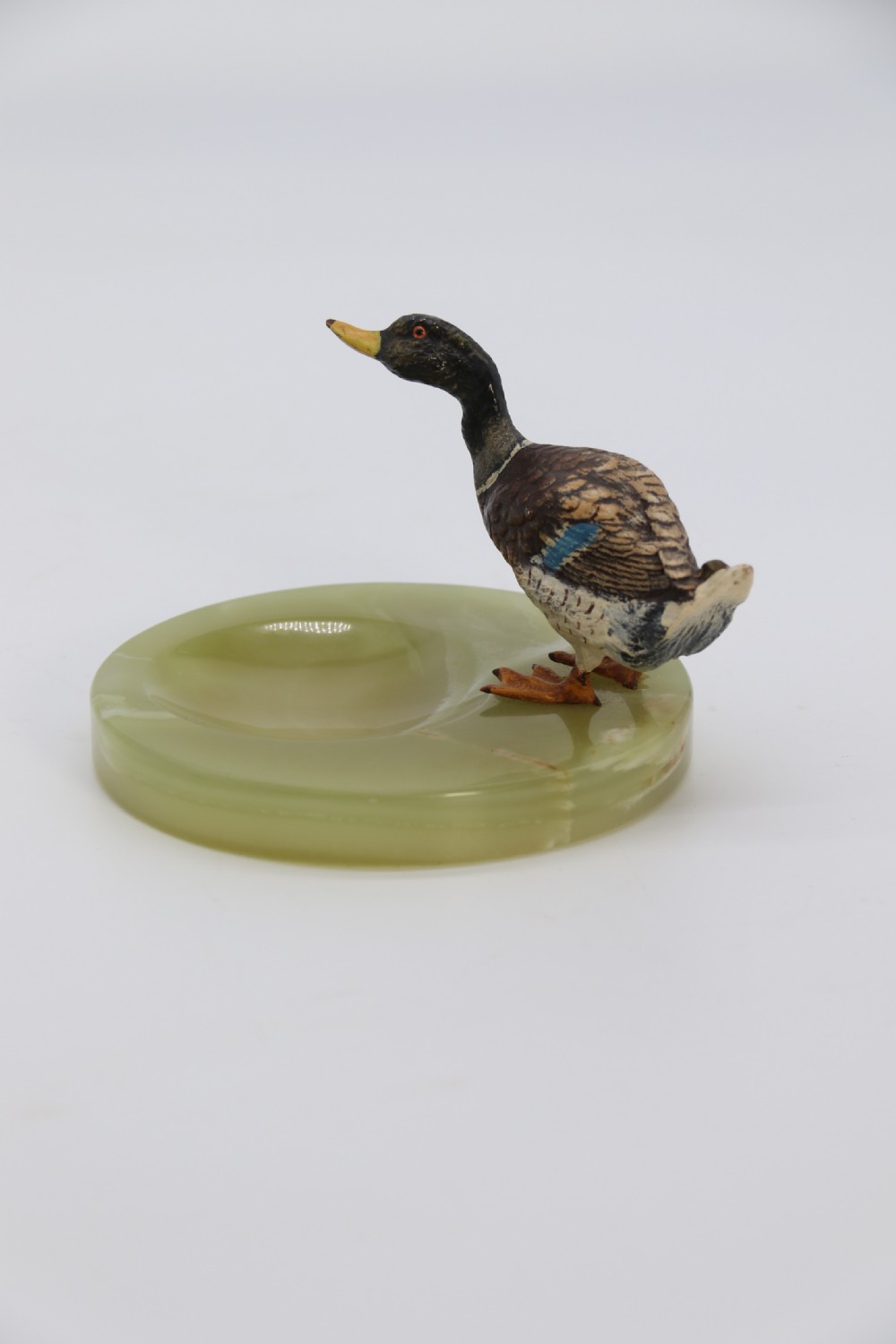 A cold painted bronze study of a mallard duck standing on the rim of a dished, circular green onyx base. View IV