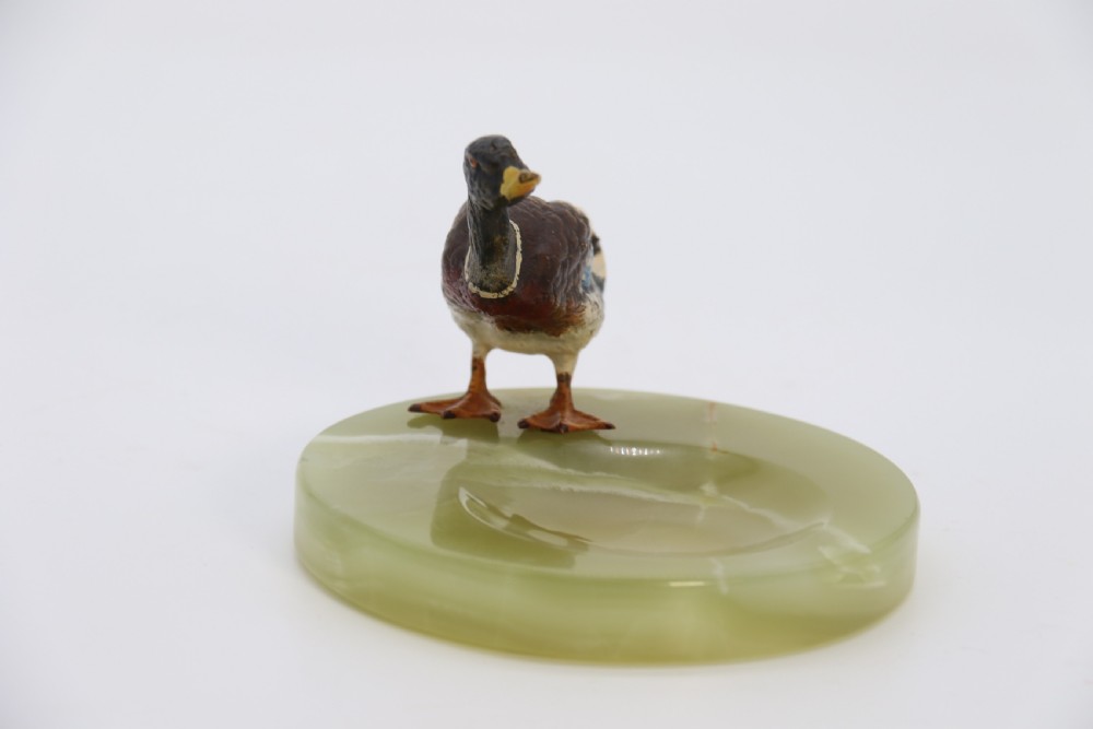 A cold painted bronze study of a mallard duck standing on the rim of a dished, circular green onyx base. View X