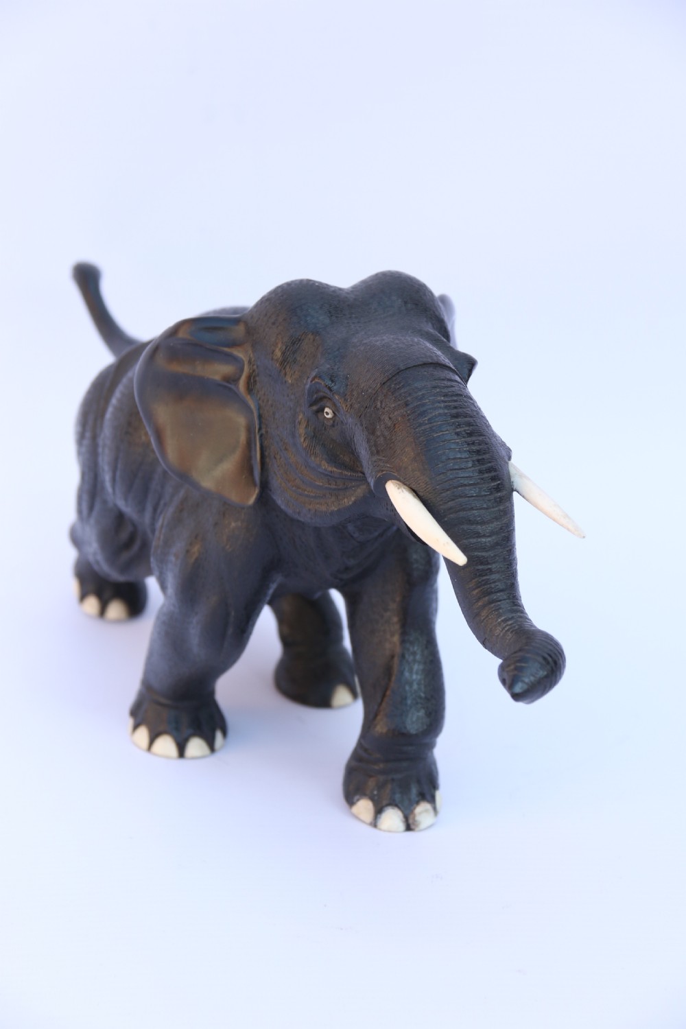 A late 19th-century hand-carved black ebony elephant sculpture shown in a striding pose with inlaid bone tusks and toenails. View III