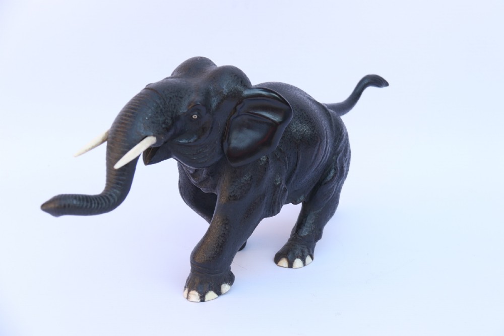 A late 19th-century hand-carved black ebony elephant sculpture shown in a striding pose with inlaid bone tusks and toenails. View V