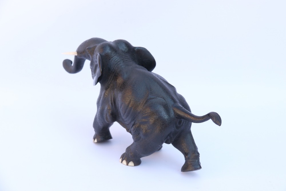 A late 19th-century hand-carved black ebony elephant sculpture shown in a striding pose with inlaid bone tusks and toenails. View VI