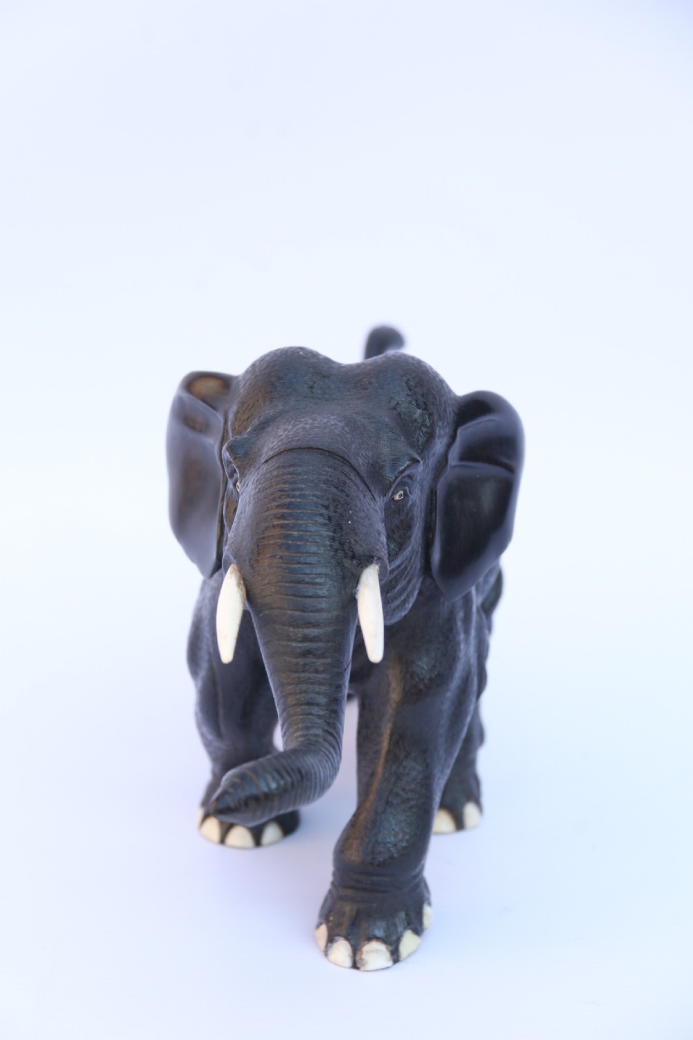 A late 19th-century hand-carved black ebony elephant sculpture shown in a striding pose with inlaid bone tusks and toenails. View VIII