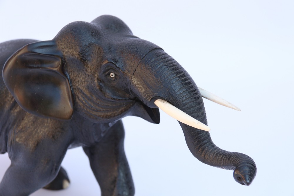 A late 19th-century hand-carved black ebony elephant sculpture shown in a striding pose with inlaid bone tusks and toenails. View IX