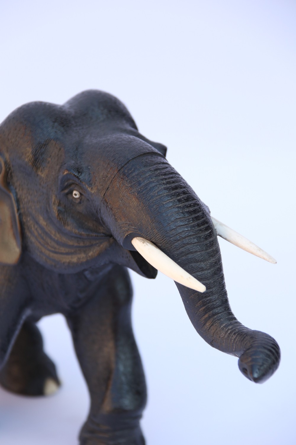 A late 19th-century hand-carved black ebony elephant sculpture shown in a striding pose with inlaid bone tusks and toenails. View X