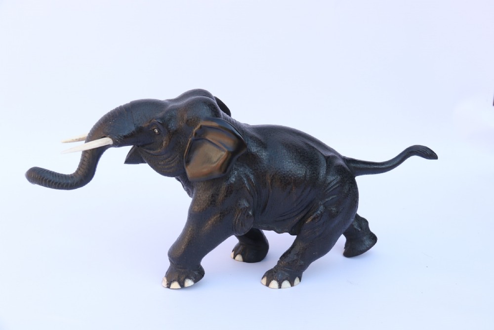 A late 19th-century hand-carved black ebony elephant sculpture shown in a striding pose with inlaid bone tusks and toenails. View XVI