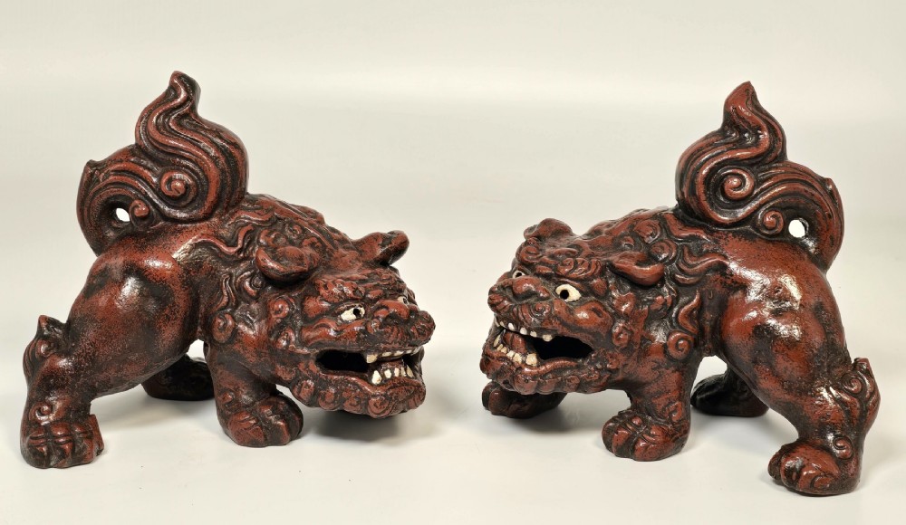 A pair of reddish-brown cast iron Chinese guardian lion figures featuring raised tails and open mouths displaying white painted teeth.