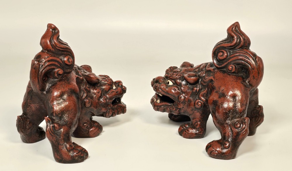 A pair of reddish-brown cast iron Chinese guardian lion figures featuring raised tails and open mouths displaying white painted teeth. View V