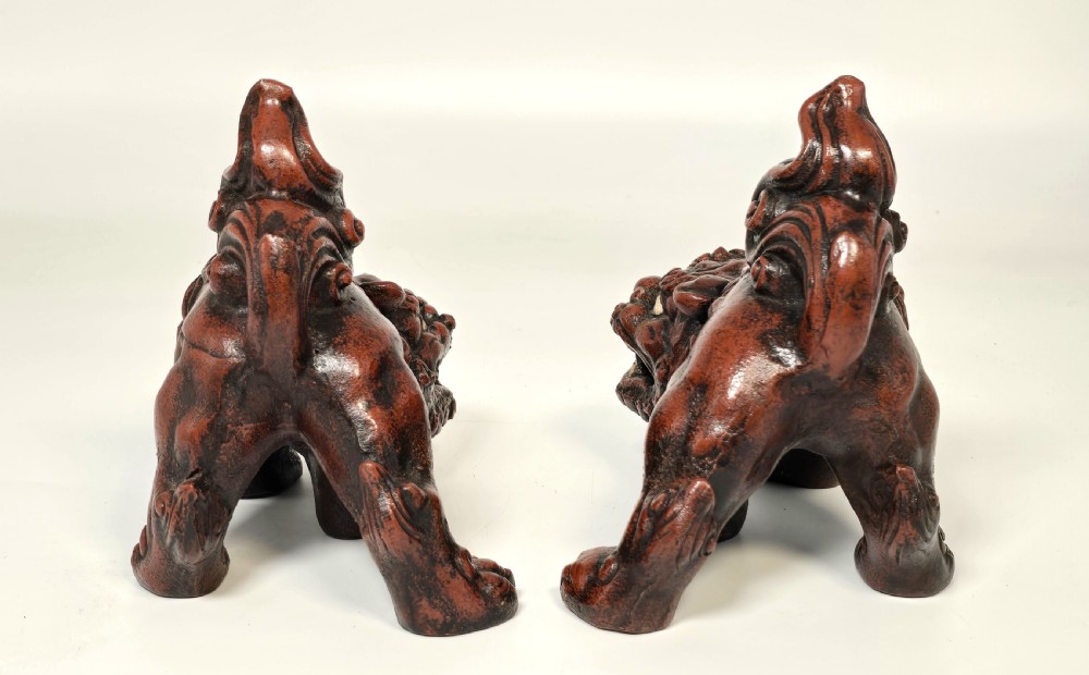 A pair of reddish-brown cast iron Chinese guardian lion figures featuring raised tails and open mouths displaying white painted teeth. View VI