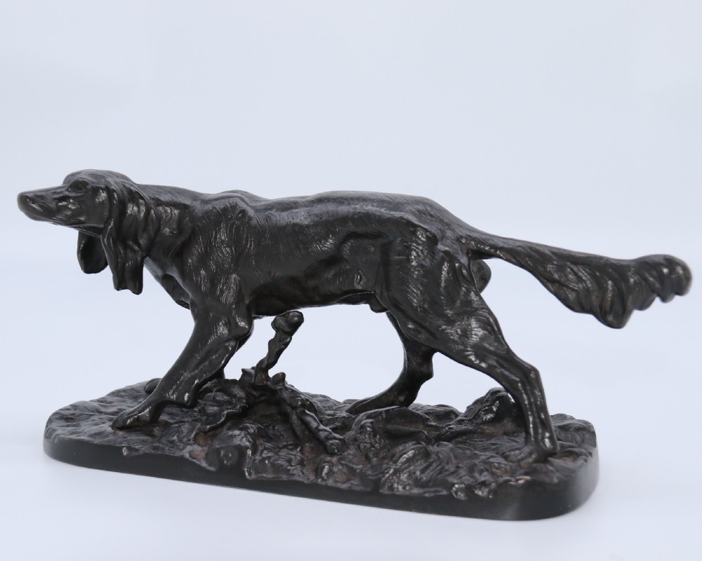 A black cast iron sculpture depicting a hunting dog walking across a naturalistic earth base. View II
