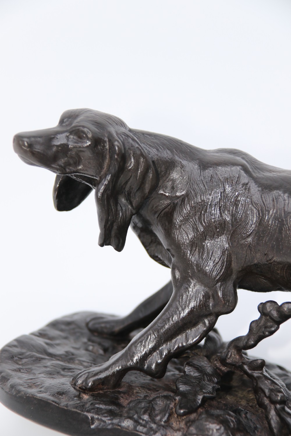 A black cast iron sculpture depicting a hunting dog walking across a naturalistic earth base. View V