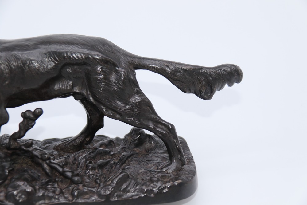 A black cast iron sculpture depicting a hunting dog walking across a naturalistic earth base. View VI