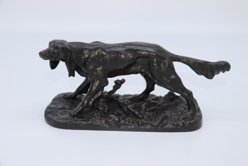 A black cast iron sculpture depicting a hunting dog walking across a naturalistic earth base. View VII