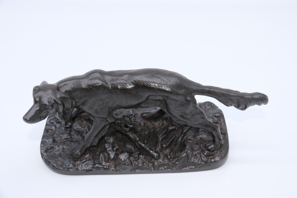 A black cast iron sculpture depicting a hunting dog walking across a naturalistic earth base. View VIII