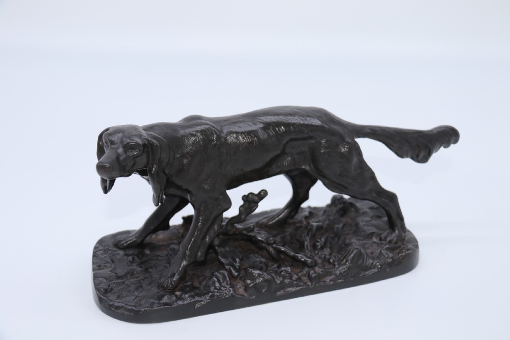 A black cast iron sculpture depicting a hunting dog walking across a naturalistic earth base. View IX