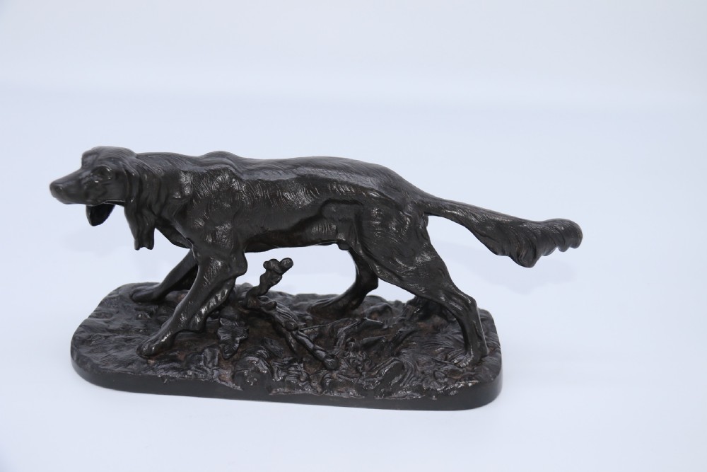 A black cast iron sculpture depicting a hunting dog walking across a naturalistic earth base. View X