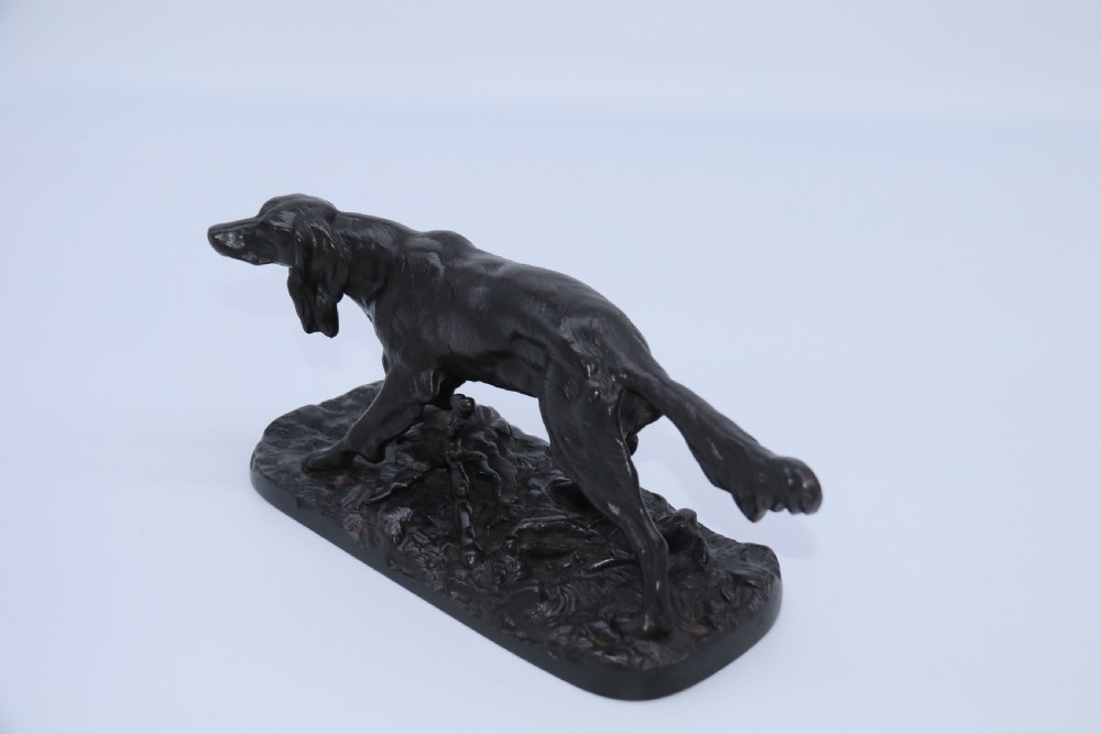 A black cast iron sculpture depicting a hunting dog walking across a naturalistic earth base. View XI