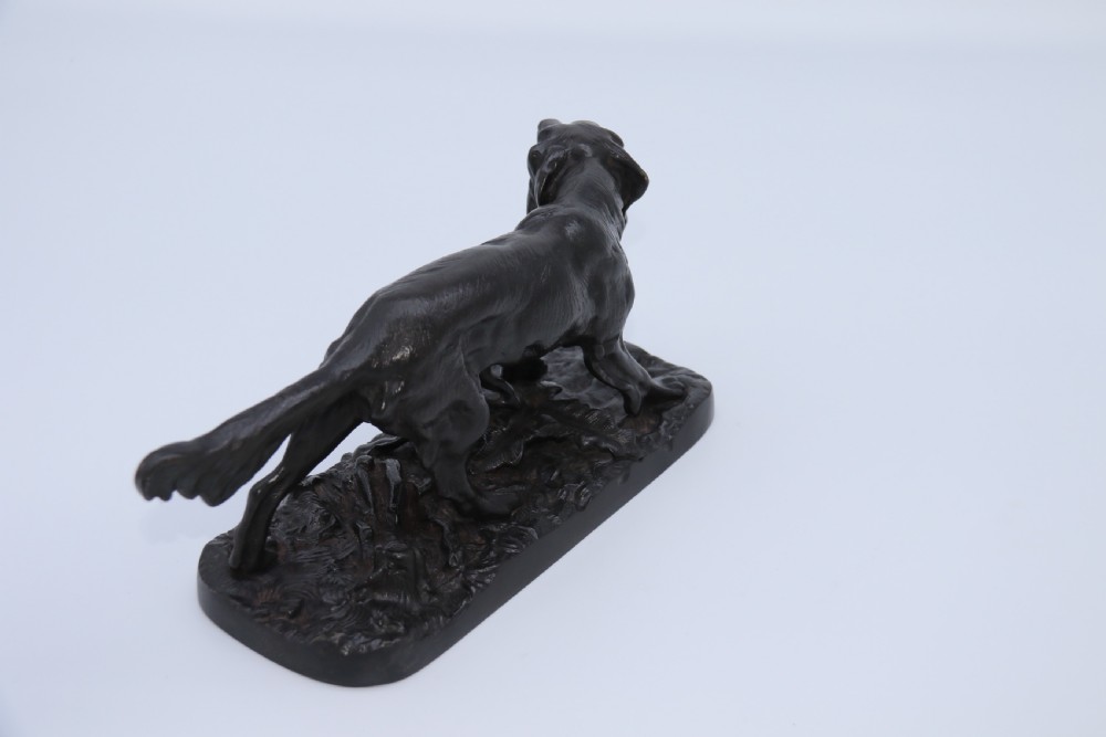 A black cast iron sculpture depicting a hunting dog walking across a naturalistic earth base. View XII