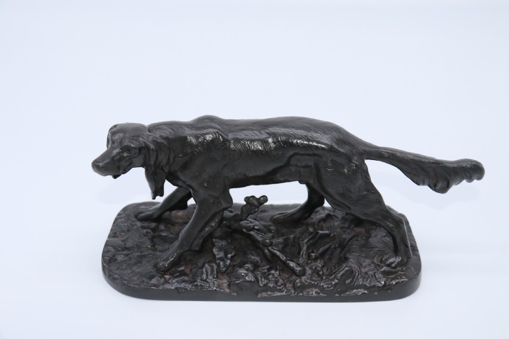 A black cast iron sculpture depicting a hunting dog walking across a naturalistic earth base. View XVIII