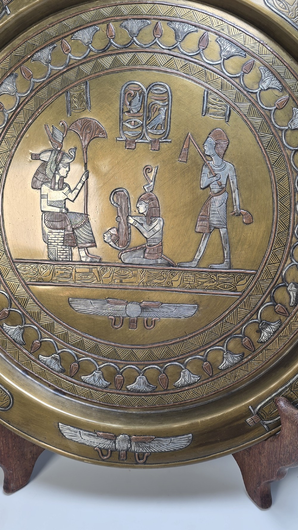 A circular brass charger featuring inlaid silver and copper depiction of Ancient Egyptian figures, hieroglyphs, and winged sun disc motifs. View III
