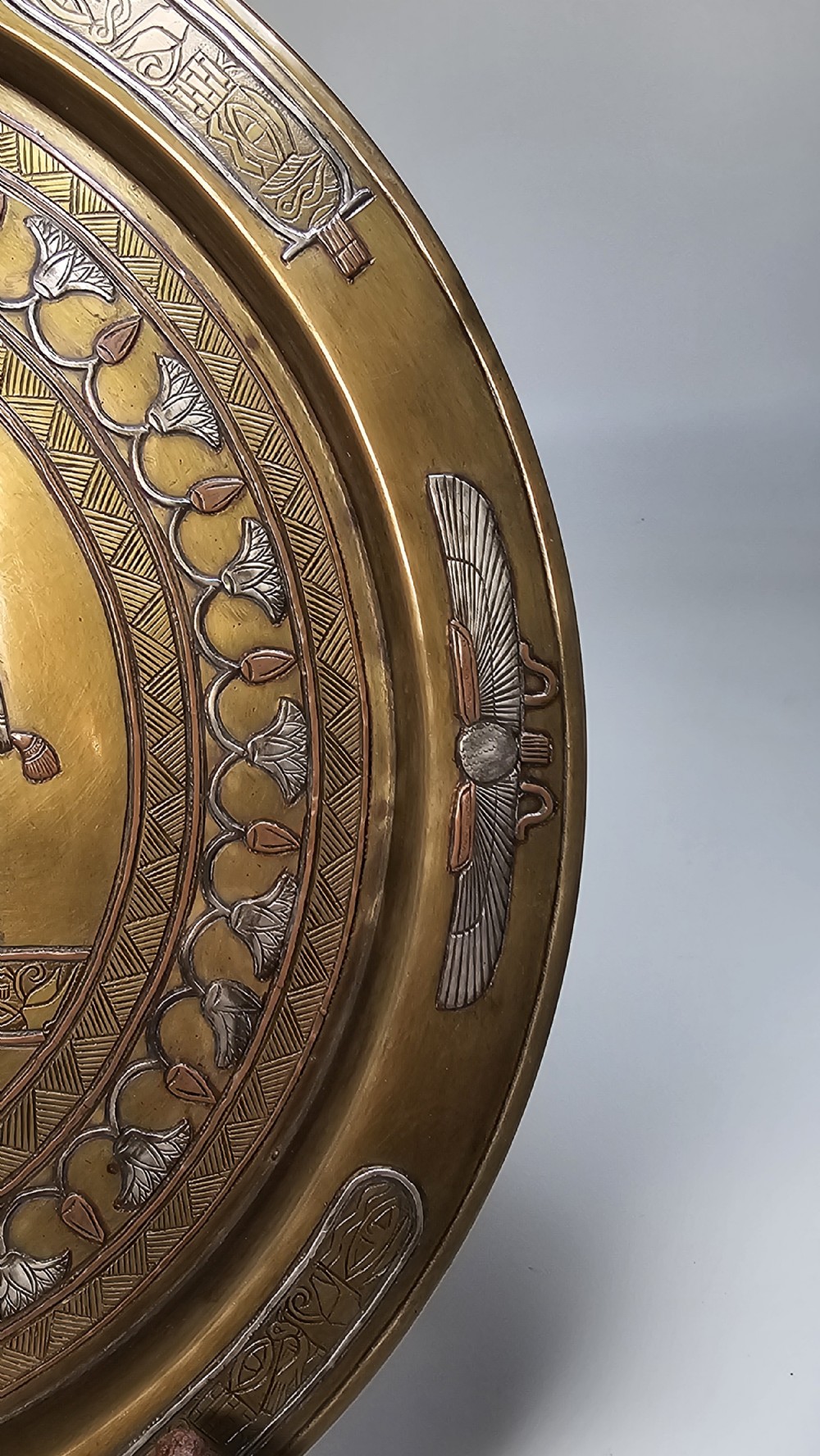 A circular brass charger featuring inlaid silver and copper depiction of Ancient Egyptian figures, hieroglyphs, and winged sun disc motifs. View VI