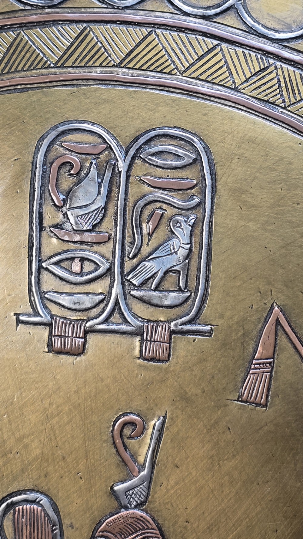 A circular brass charger featuring inlaid silver and copper depiction of Ancient Egyptian figures, hieroglyphs, and winged sun disc motifs. View XI