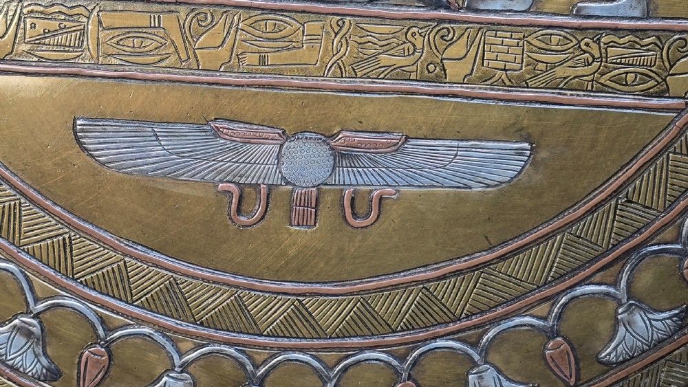 A circular brass charger featuring inlaid silver and copper depiction of Ancient Egyptian figures, hieroglyphs, and winged sun disc motifs. View XIII