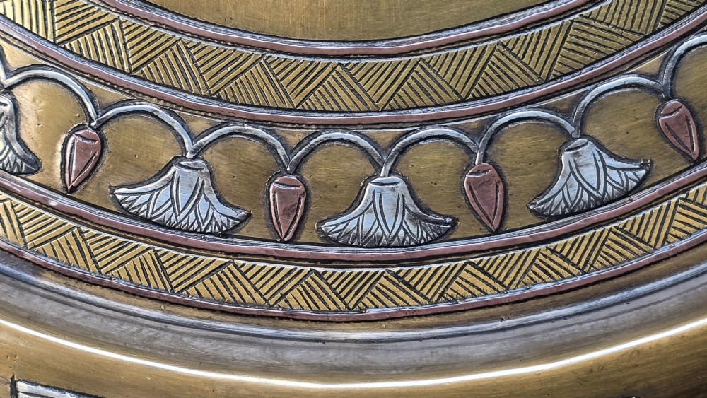 A circular brass charger featuring inlaid silver and copper depiction of Ancient Egyptian figures, hieroglyphs, and winged sun disc motifs. View XIV