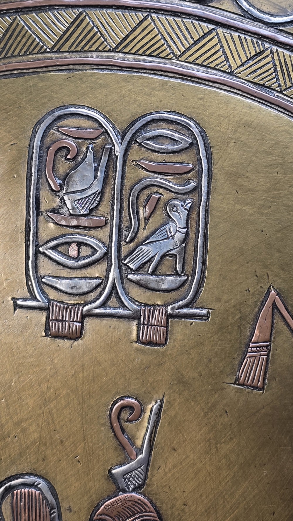 A circular brass charger featuring inlaid silver and copper depiction of Ancient Egyptian figures, hieroglyphs, and winged sun disc motifs. View XVIII