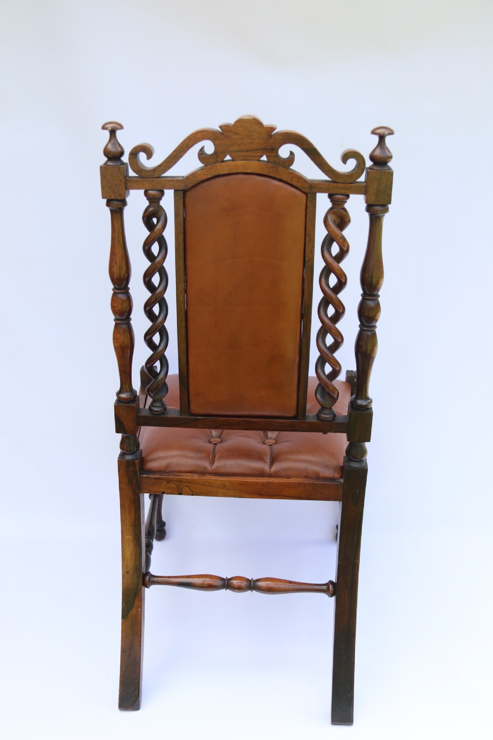 An early Victorian childs chair crafted from carved rosewood with barley twist columns, turned legs, and button-tufted brown leather upholstery on the seat and backrest. View X